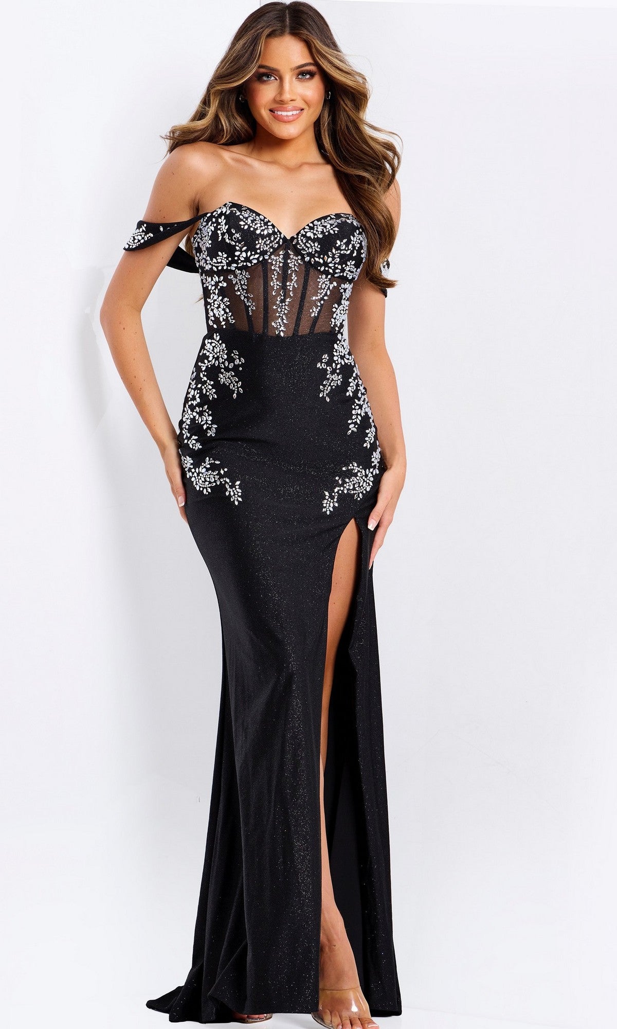 A woman poses against a plain white background wearing the Jovani 49659 long prom dress in black/silver with an off-the-shoulder neckline, sheer bodice, beaded appliques, and a thigh-high slit.